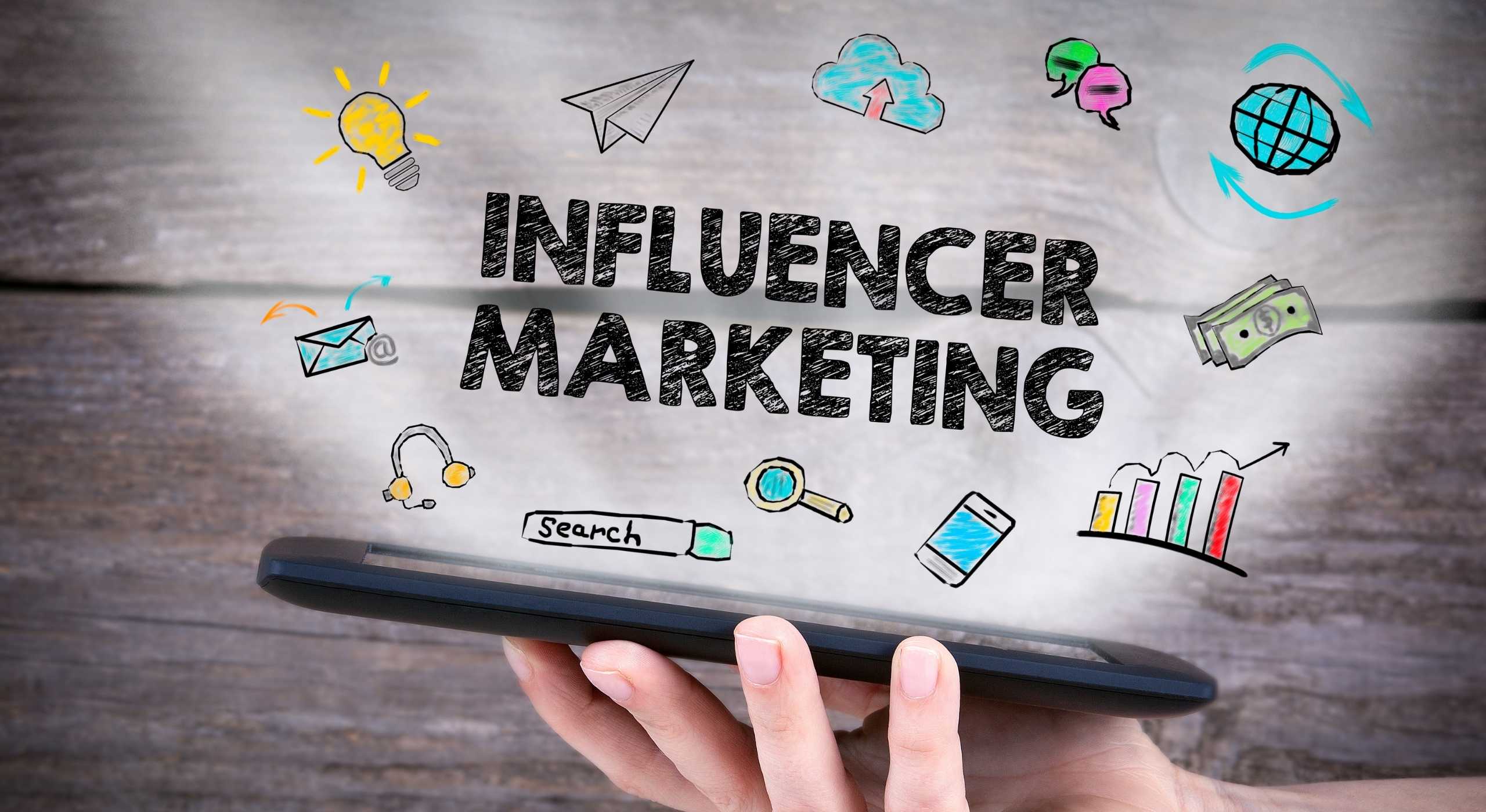 Image shows a hand holding a tablet with the words "Influencer Marketing" written on the screen.