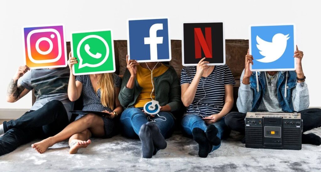 The image shows five people sitting on the floor with their faces covered by social media logos. The logos are for Instagram, WhatsApp, Facebook, Netflix, and Twitter.
