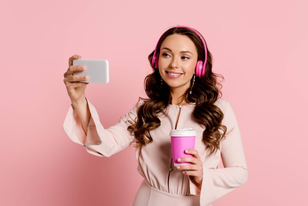 A young woman with holding a white phone in her right hand and a pink coffee cup in her left hand and doing tiktok