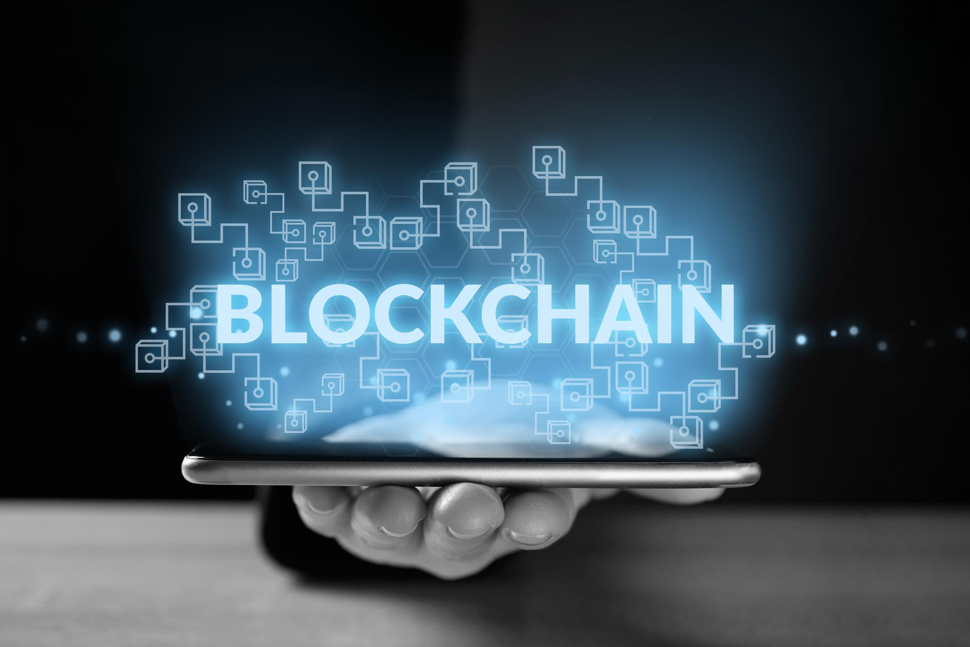 blockchain in digital marketing - picture include the mobile phone on a human hand and it's srcreen light display 'BLOCKCHAIN' word.