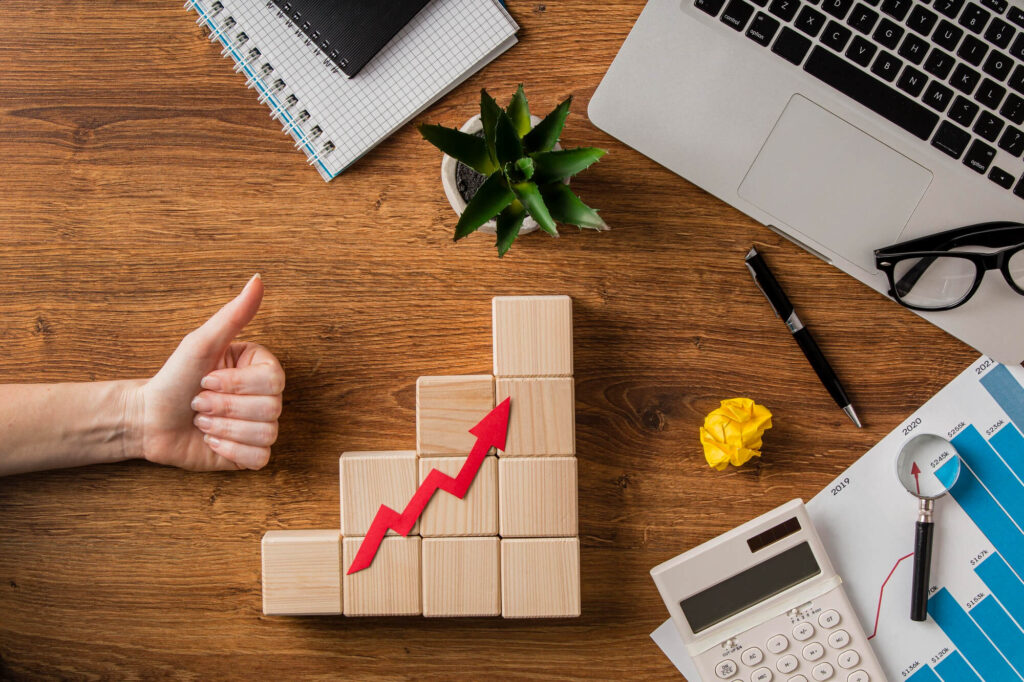 A Person's hand giving a thumbs up next to wooden blocks and a graph on a desk - Webco Marketing Blogs